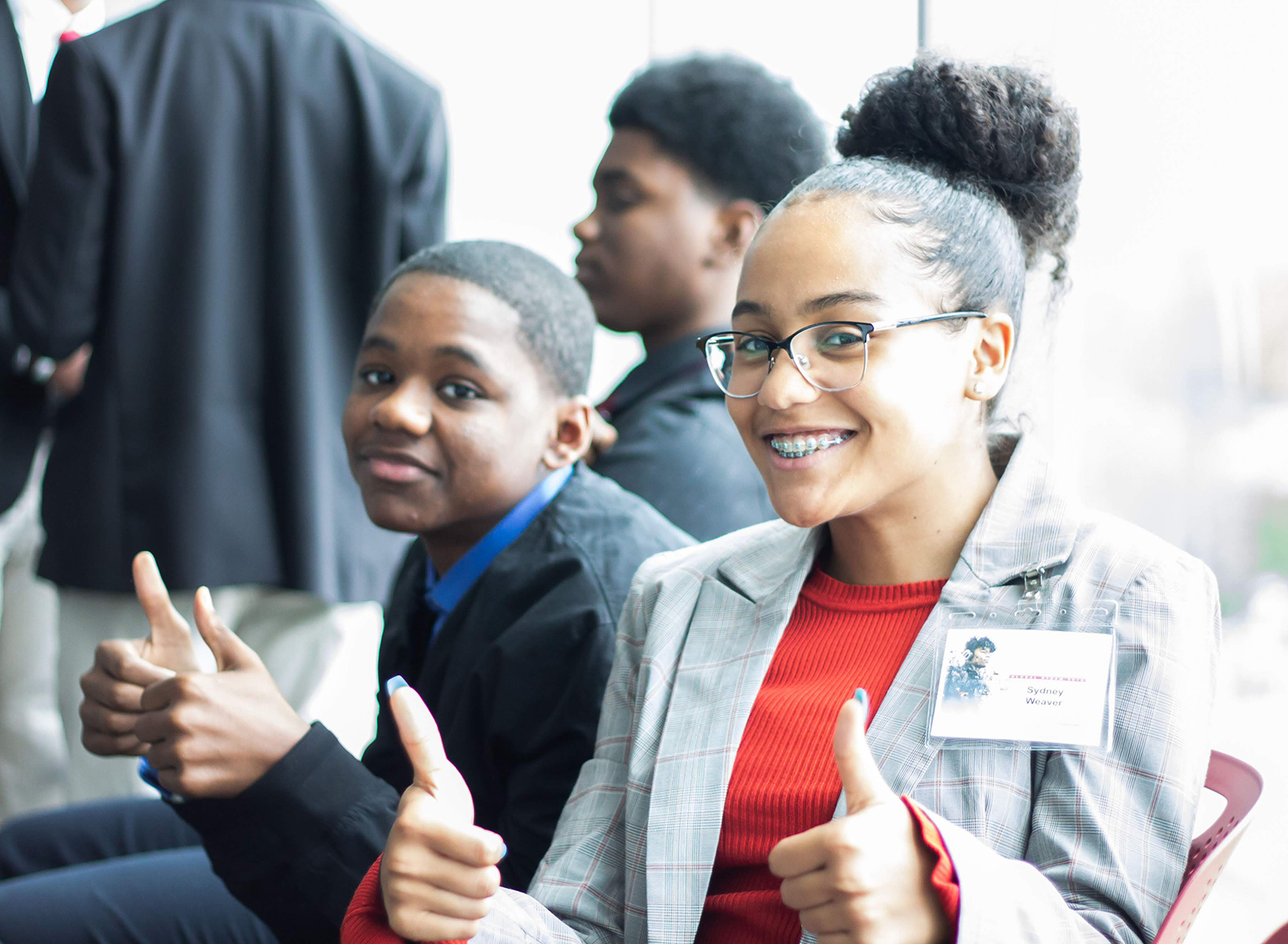 Two students at a conference smiling. One student has two thumbs up
